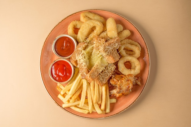 Frietjes, uienringen, kippenvleugels, beschuit, een snack tot bier op een groot bord met twee sauzen op een bruine achtergrond. bovenaanzicht.