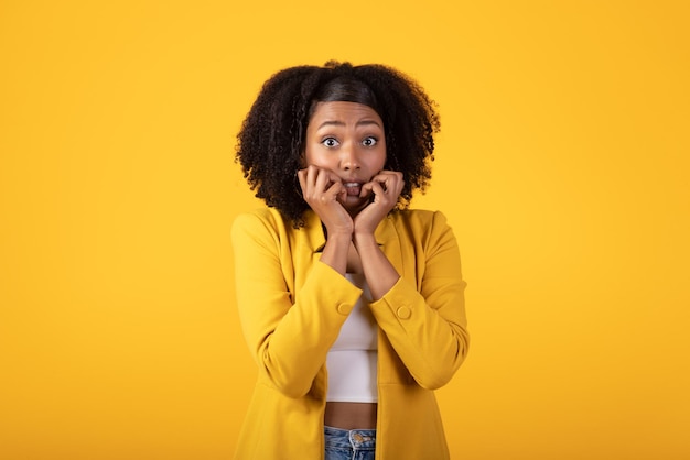 Frightened young black bushy curly lady looking at camera isolated on yellow background studio shot