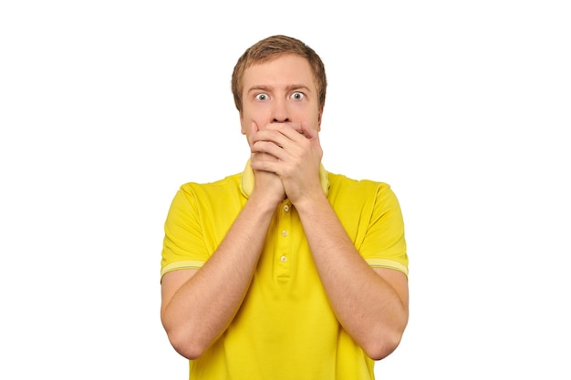 Frightened young man in yellow Tshirt holding hands over face white background afraid negative