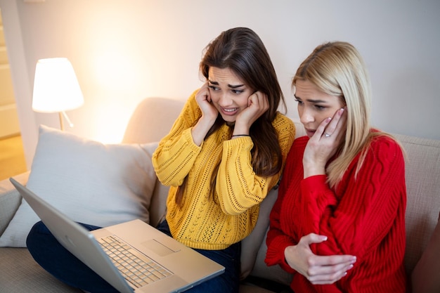 Frightened young women watching movie at home girls watching a\
terror scary movie on tv sitting on a couch at home