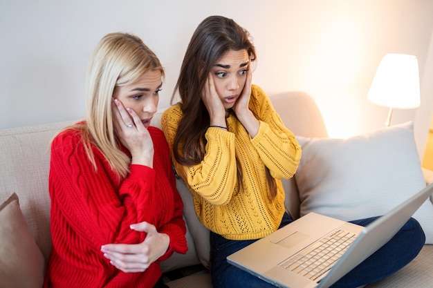 Frightened young women watching movie at home Girls watching a terror scary movie on tv sitting on a couch at home