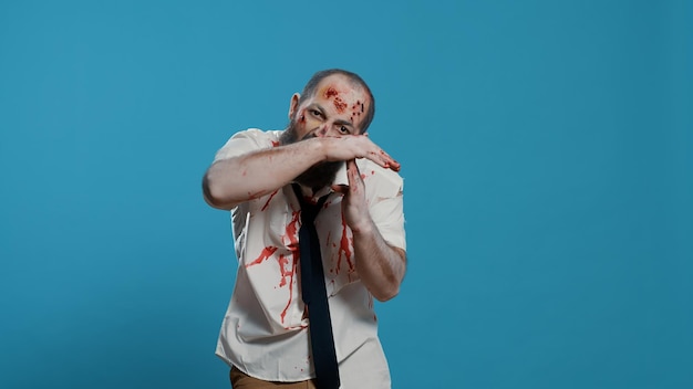 Frightening evil looking zombie making timeout hand gesture on blue background. Scary mindless brain-eating apocalyptic monster doing break time hand signal while looking at camera. Studio shot