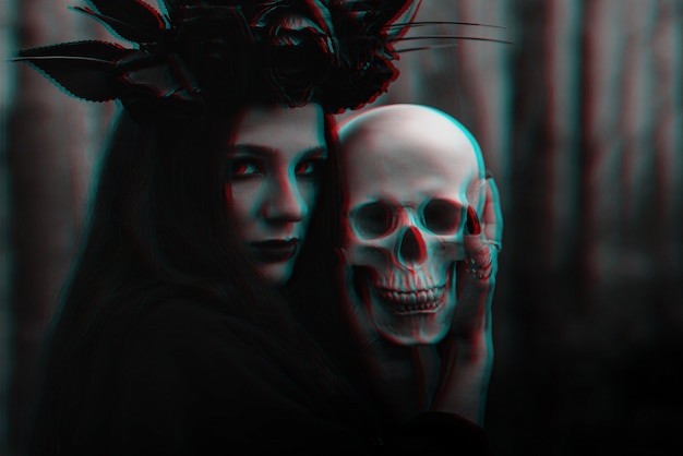 Photo frightening evil witch in black rags holds a dead man's skull in her hands for a dark ritual. black and white with 3d glitch virtual reality effect