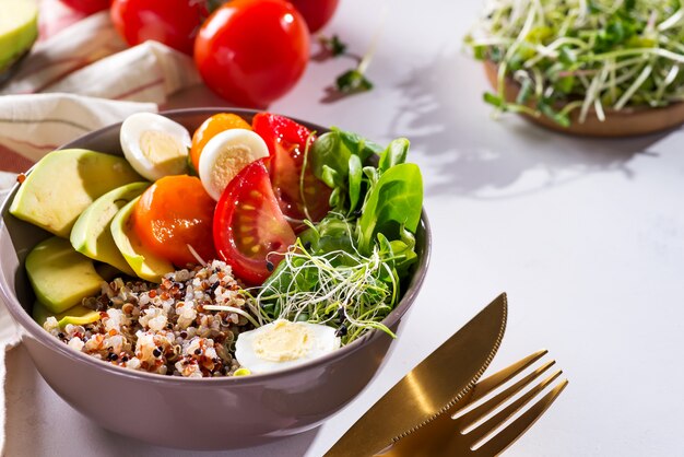 Frisse gezonde salade met quinoa, cherrytomaten en gemengde greens, avocado, ei en micro greens op marmer