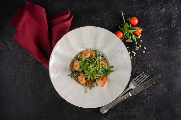 Frisse groene salade met gebakken garnalen, kerstomaatjes en rucola in een diepe plaat. Bovenaanzicht.