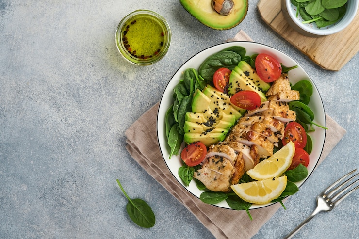 Foto frisse groene salade met gegrilde kipfilet, spinazie, tomaten, avocado, citroen en zwarte sesamzaadjes, olijfolie in witte kom op lichte leisteen achtergrond. voeding dieet concept. bovenaanzicht. kopieer ruimte