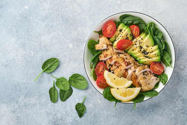 Foto frisse groene salade met gegrilde kipfilet, spinazie, tomaten, avocado, citroen en zwarte sesamzaadjes, olijfolie in witte kom op lichte leisteen achtergrond. voeding dieet concept. bovenaanzicht. kopieer ruimte