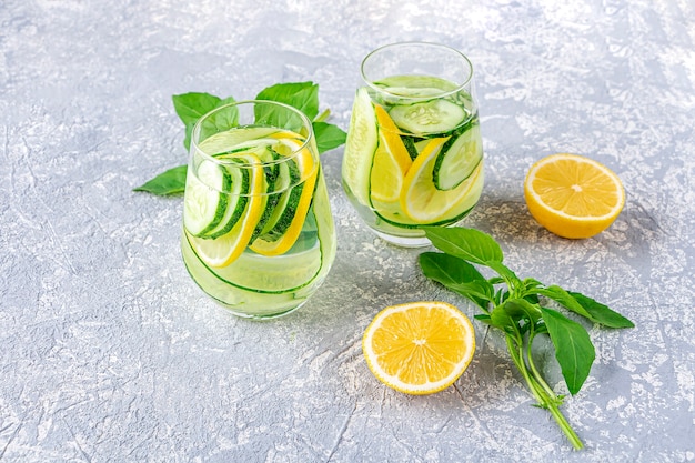 Frisse koele detox waterdrank met komkommer en citroen. Twee glazen limonade met basilicum en muntblaadjes. Concept van goede voeding en gezond eten. Fitness dieet.