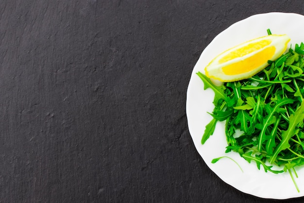 Frisse lentesalade met rucola en citroen, in kom op donkere stenen achtergrond met vrije tekstruimte.