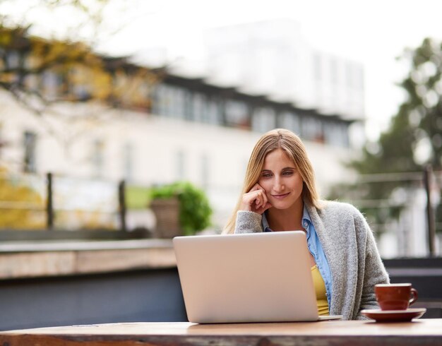 Frisse lucht en gratis wifi Bijgesneden opname van een aantrekkelijke jonge vrouw die haar laptop gebruikt in een openluchtkoffieshop