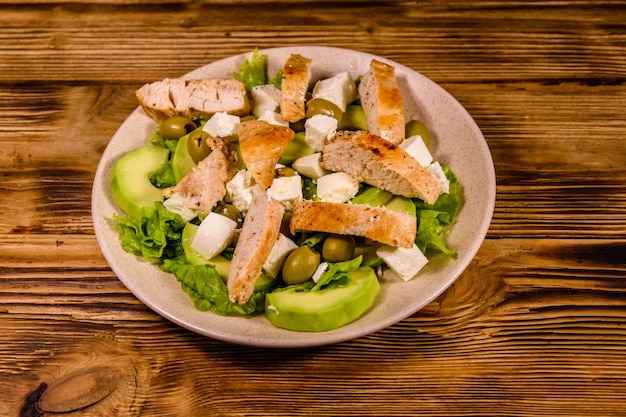 Frisse salade met kippenvlees feta kaas avocado groene olijven en sla bladeren in keramische plaat op houten tafel