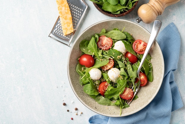 Frisse salade met rucola kerstomaatjes, mozzarella kaas en harde kaas op witte houten ondergrond Top view