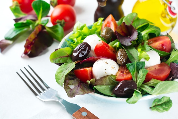 Frisse salade met sla, cresssalade, rucola, bieten, tomaten, mazarellakaas en olijven in een keramische mok op een lichte ondergrond. gezond eten. selectieve aandacht