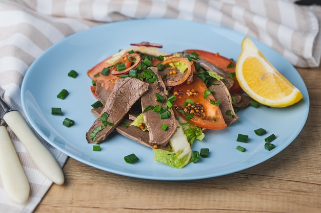 Frisse salade met varkenshart, sla, tomaat, groene ui en citroen in blauwe plaat op houten tafel