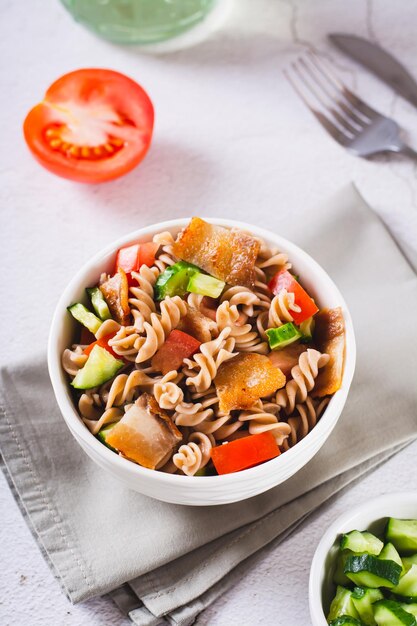 Frisse salade van boekweitpasta, tomaten, komkommers en gebakken spek in een kom verticaal zicht