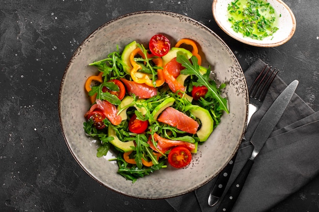 Frisse zomerse groentesalade met rucola, tomaten, paprika, avocado en zalm op een bord bovenaanzicht.