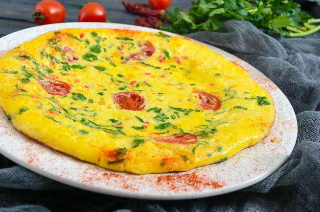 Frittata. italiaanse omelet met kaas, groenen en tomaten op een witte plaat op een houten achtergrond.