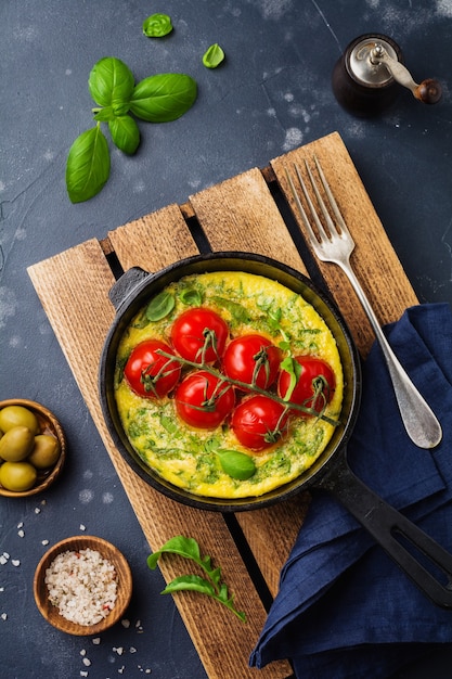 Frittata met rucola, aardappelen en kerstomaatjes in ijzeren pan op oude stenen tafel. Bovenaanzicht.