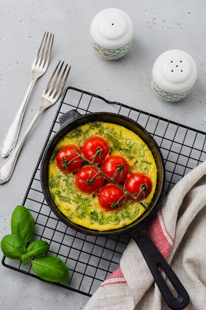 Frittata met rucola, aardappelen en kerstomaatjes in ijzeren pan op oude stenen tafel. Bovenaanzicht.