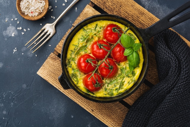 Frittata with arugula, potatoes and cherry tomatoes in iron pan on old stone table background