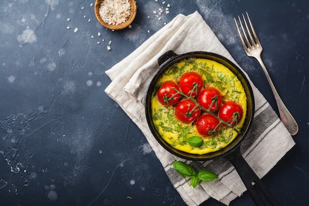 Frittata with arugula, potatoes and cherry tomatoes in iron pan on old stone table table.