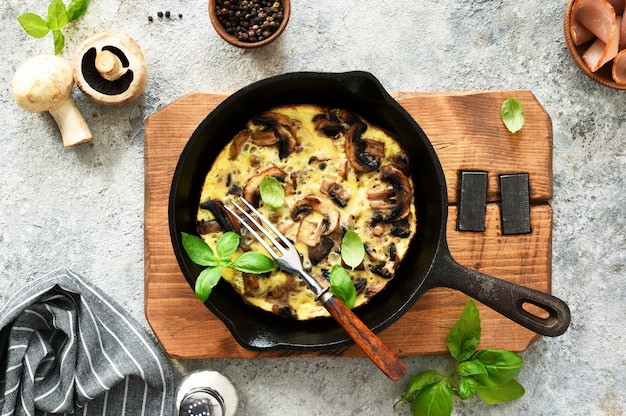 Frittata ai funghi in padella con basilico su fondo in cemento. fritata è un piatto della colazione italiana.