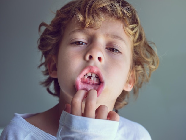 From below of adorable kid with curly blond hair and brown eyes demonstrating open mouth with one lost milk tooth while touching lip and looking at camera