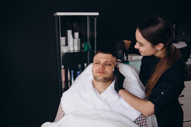 From above anonymous beautician in latex gloves injecting botulinum toxin into forehead of bearded young male client during cosmetology session in beauty studio