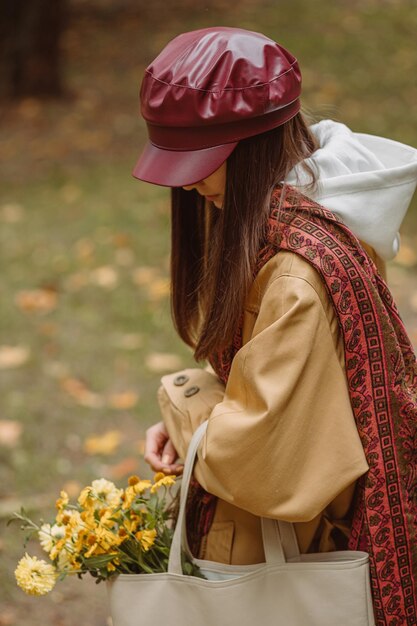 From above of anonymous woman with flowers in bag walking in park in autumn season