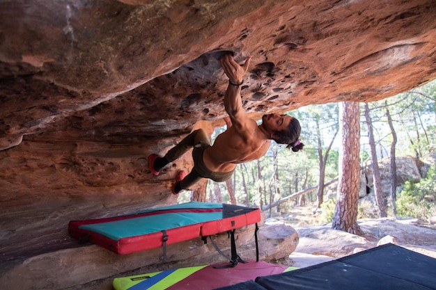 From below back view of young sportsman with naked torso climbing natural rocky roof