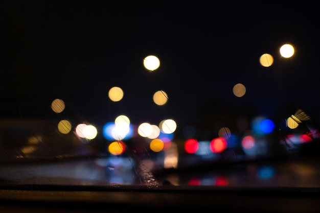 From a car windshield with windshield wipers in action Blurry lights outside in the night