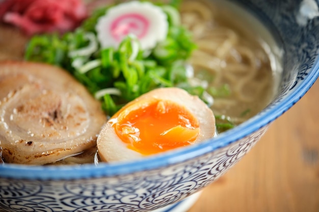 From above closeup of appetizing fresh ramen soup with egg and onion in ceramic bowl served on wooden table