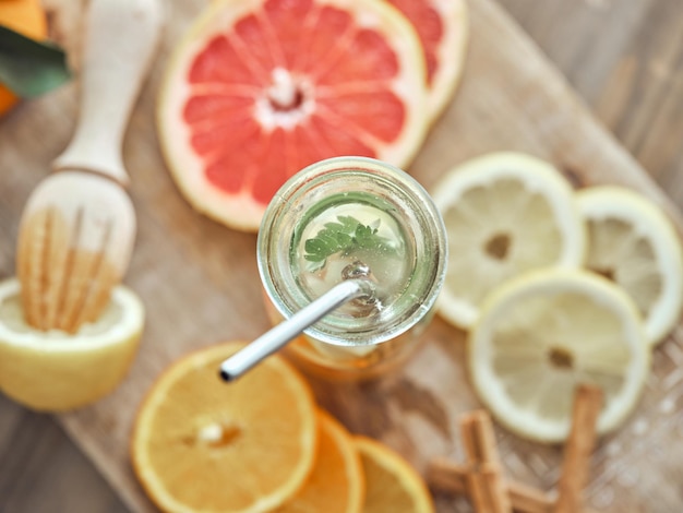 From above composition of bottle with zero waste straw filled with refreshing drink served with slices of various citruses and cinnamon sticks on wooden cutting board