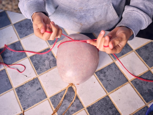 From above of crop anonymous female tying with red twine sausage in pork guts casing prepared for drying in village of Matanza in Mallorca