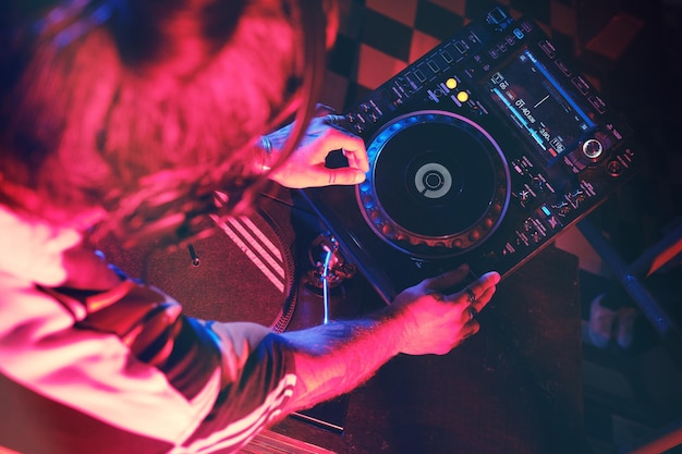 희미한 조명이 있는 나이트클럽에서 작업하는 동안 현대적인 CDJ 플레이어에서 노래를 연주하는 익명의 재능 있는 DJ의 위에서