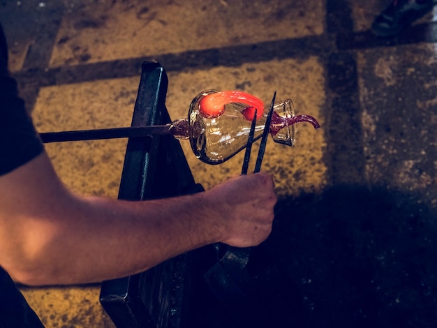 From above of crop unrecognizable male artisan making glass decanter with handle while working in workshop