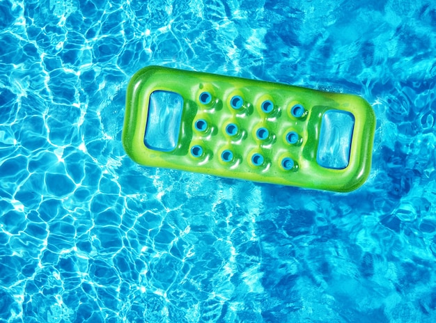 Сверху вид с дрона на ярко-зеленый надувной матрас, плавающий на голубой поверхности бассейна в солнечном свете в летнее время