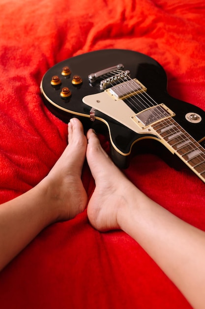 From above of female guitarist sitting barefoot on bed with electric musical instrument at home