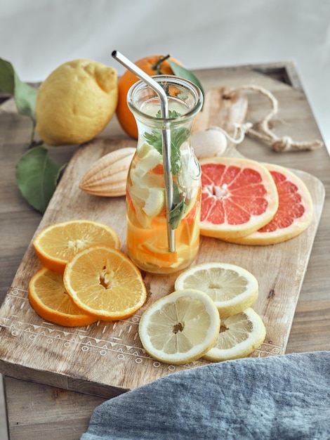 From above glass filled with fresh detox lemonade and sliced citruses on wooden cutting board