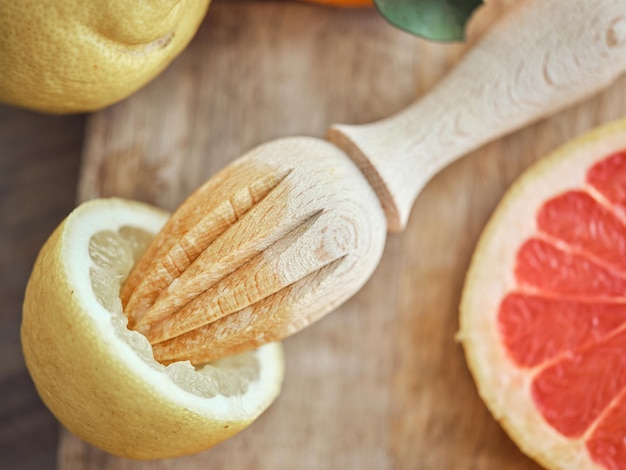 From above half of lemon with manual wooden juicer on cutting board with slice of fresh pomelo in light kitchen