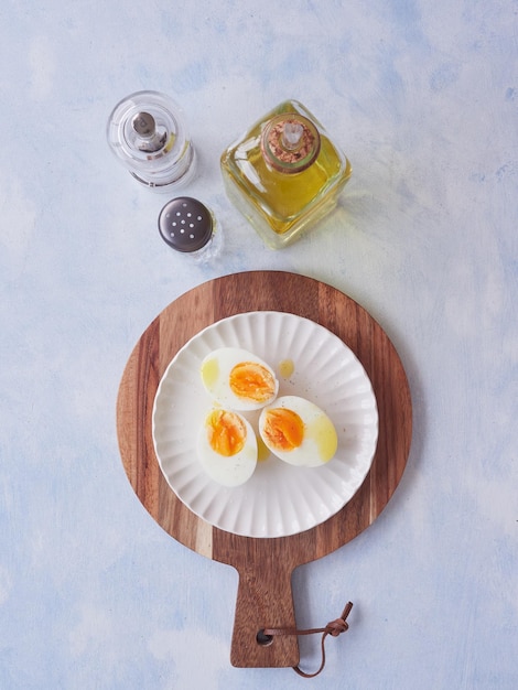 from above halves of hard boiled eggs with olive oil and pepper on a white plate on a round wooden cutting board