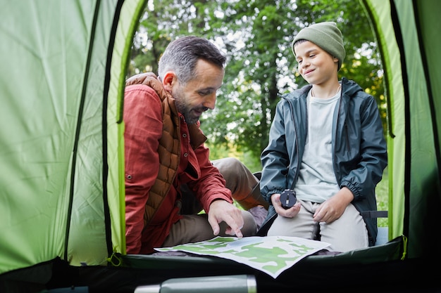 写真 森でのキャンプ旅行中にテントのそばに座っている成熟した父と息子の内側のショットから、スペースをコピーします