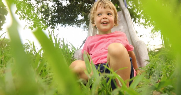 From below of little boy on slide in green grass having fun on playground