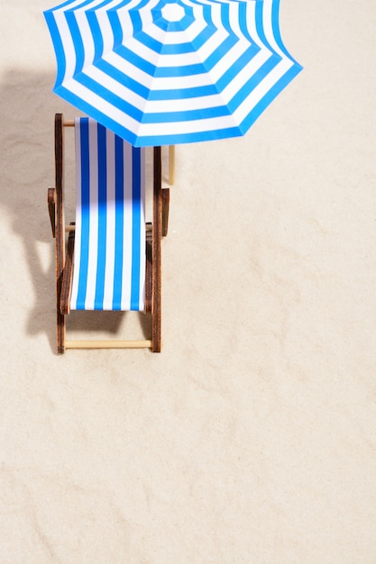 Сверху лаунж-зоны на пляже с полосатым креслом под зонтиком.
