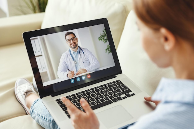 From above modern female sitting on couch and making video call\
to medical practitioner from home