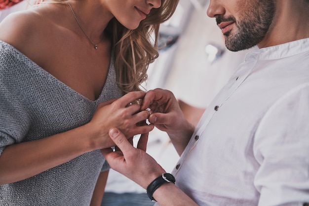 From now and forever. Close up of young man taking on engagement ring on his girlfriend's finger while standing in the bedroom