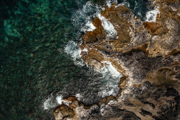 From above of ocean coastline with rough dashing waves of clear water in daylight