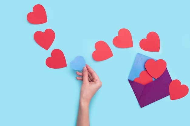 Из одного конверта выходит много красных сердечек с одним синим сердечком, которое держит в себе рука девушки.