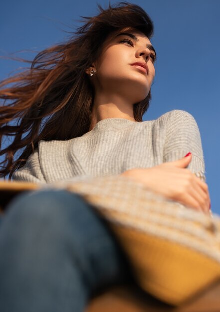 From below of pensive charming female in knitted sweater looking away in thoughts