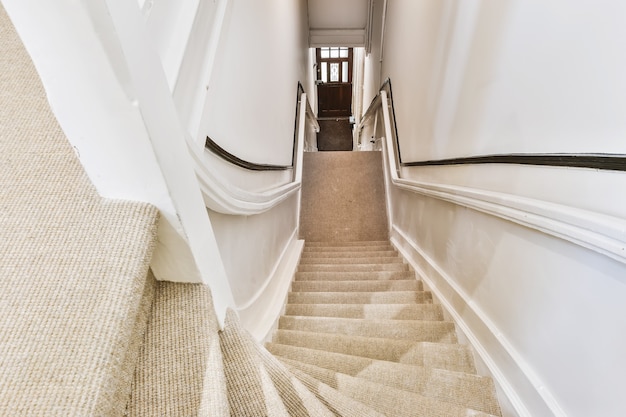 Photo from below perspective view of stairway to upper storey with handrails and carpet on steps